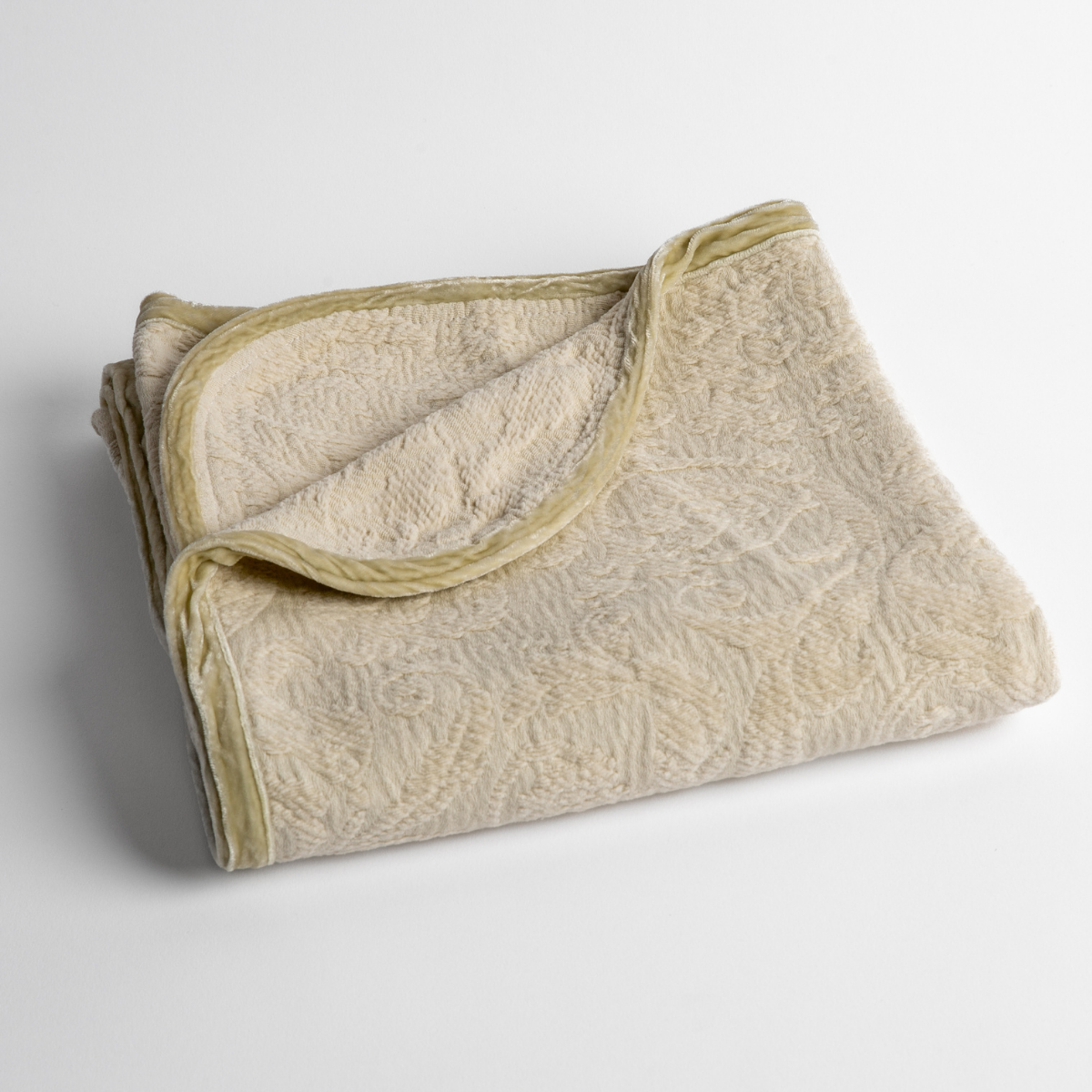 Parchment: a folded blanket with the corner turned down to show the trim against a white background, shot from an overhead angle.