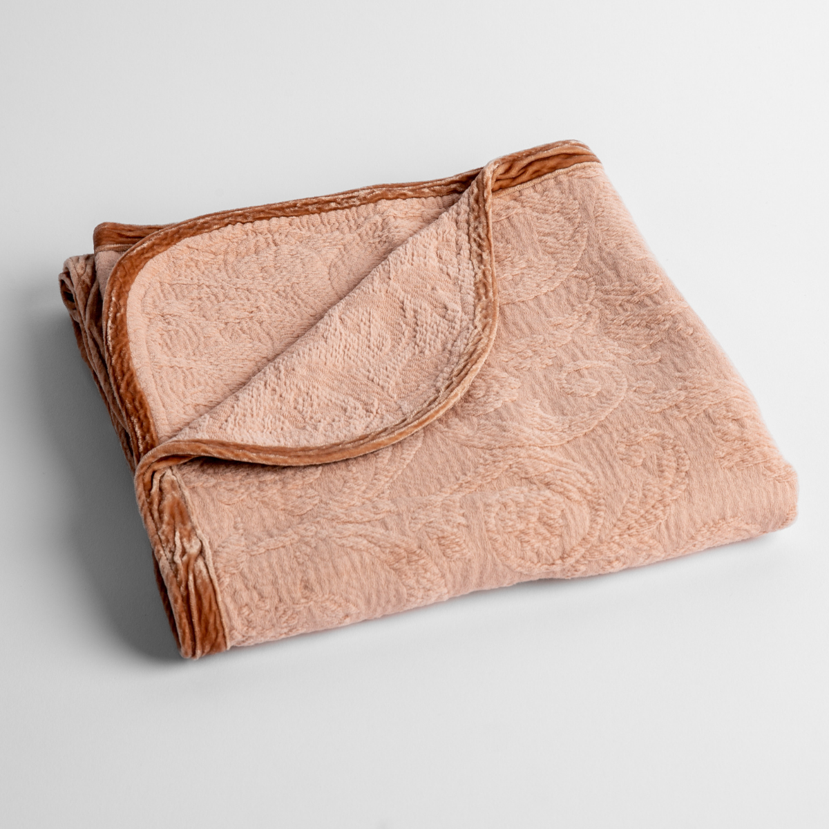 Rouge: a folded blanket with the corner turned down to show the trim against a white background, shot from an overhead angle.