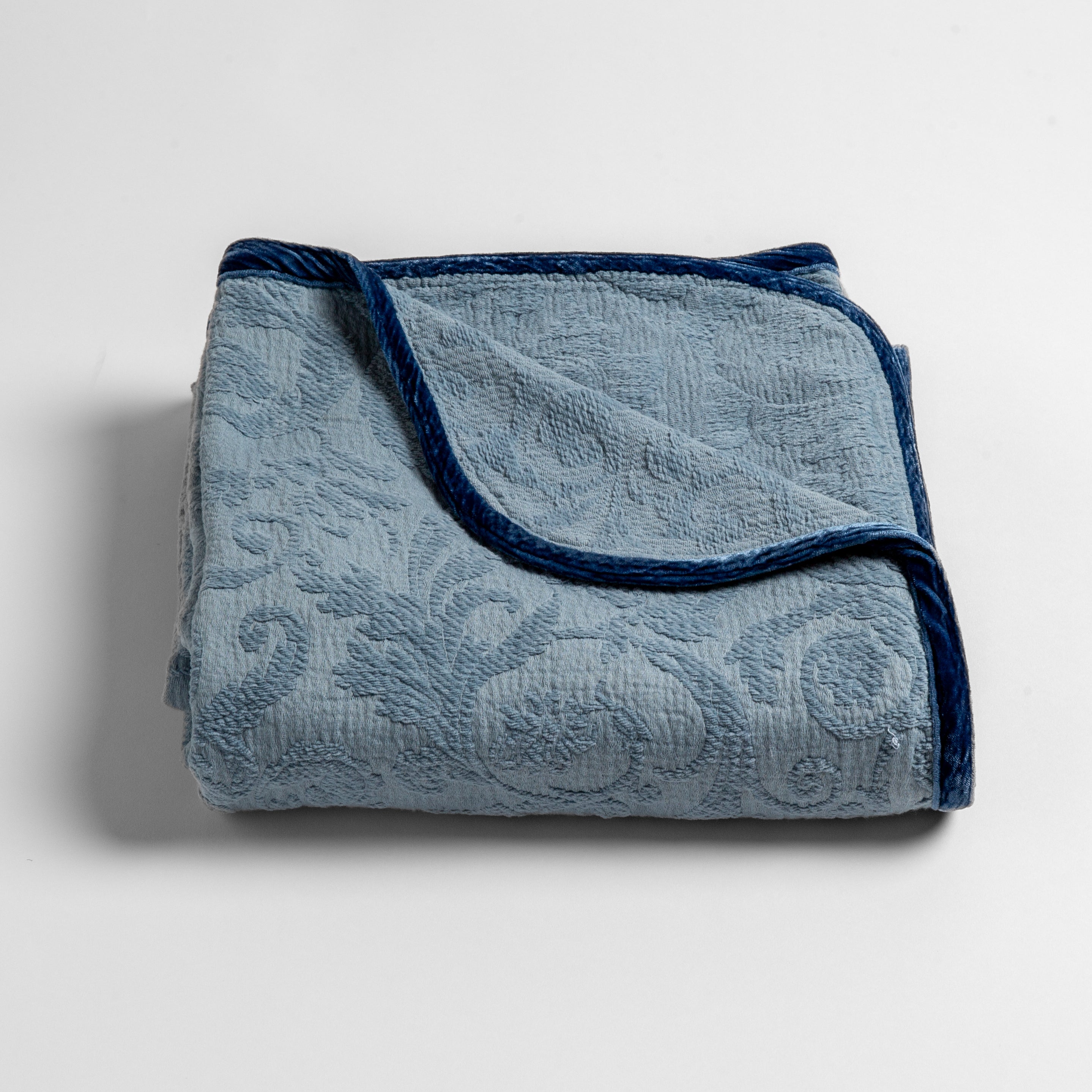 Tahoe Blue: a folded blanket with the corner turned down to show the trim against a white background, shot from an overhead angle.