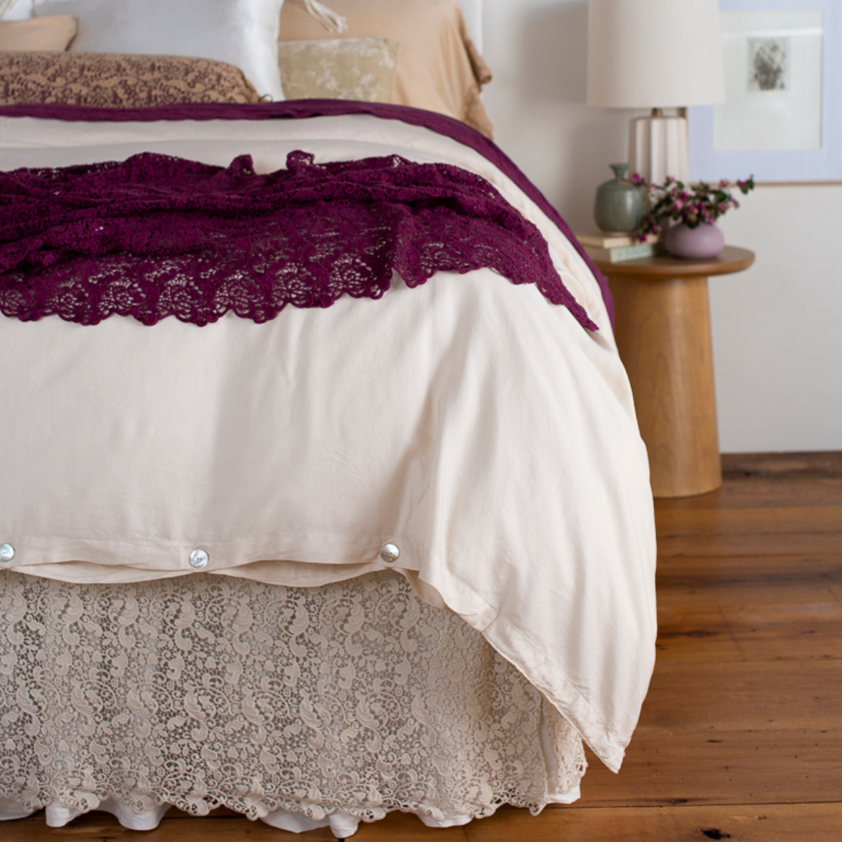 : cotton lace bed skirt and bed scarf shown from the foot of the bed dressed in light tones with pops of color.
