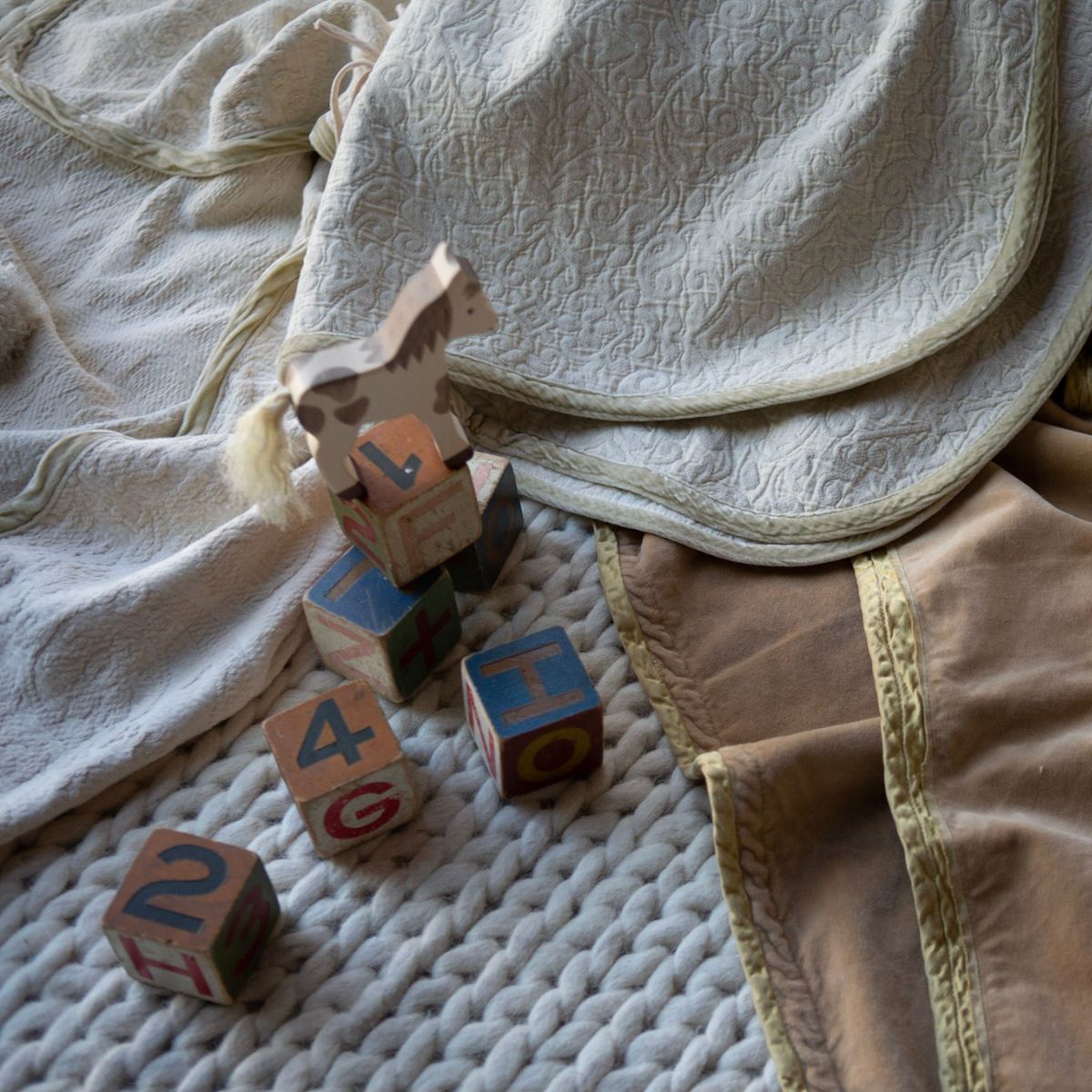 : three baby blankets strewn on the floor with wooden toys scattered on a braided rug.