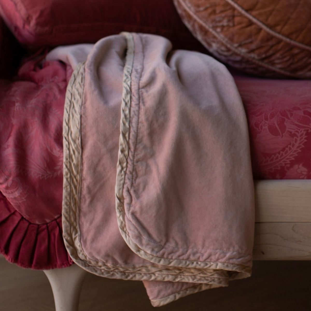 : cotton velvet baby blanket trimmed in charmeuse shown close up on a toddler bed with vibrant red tones.