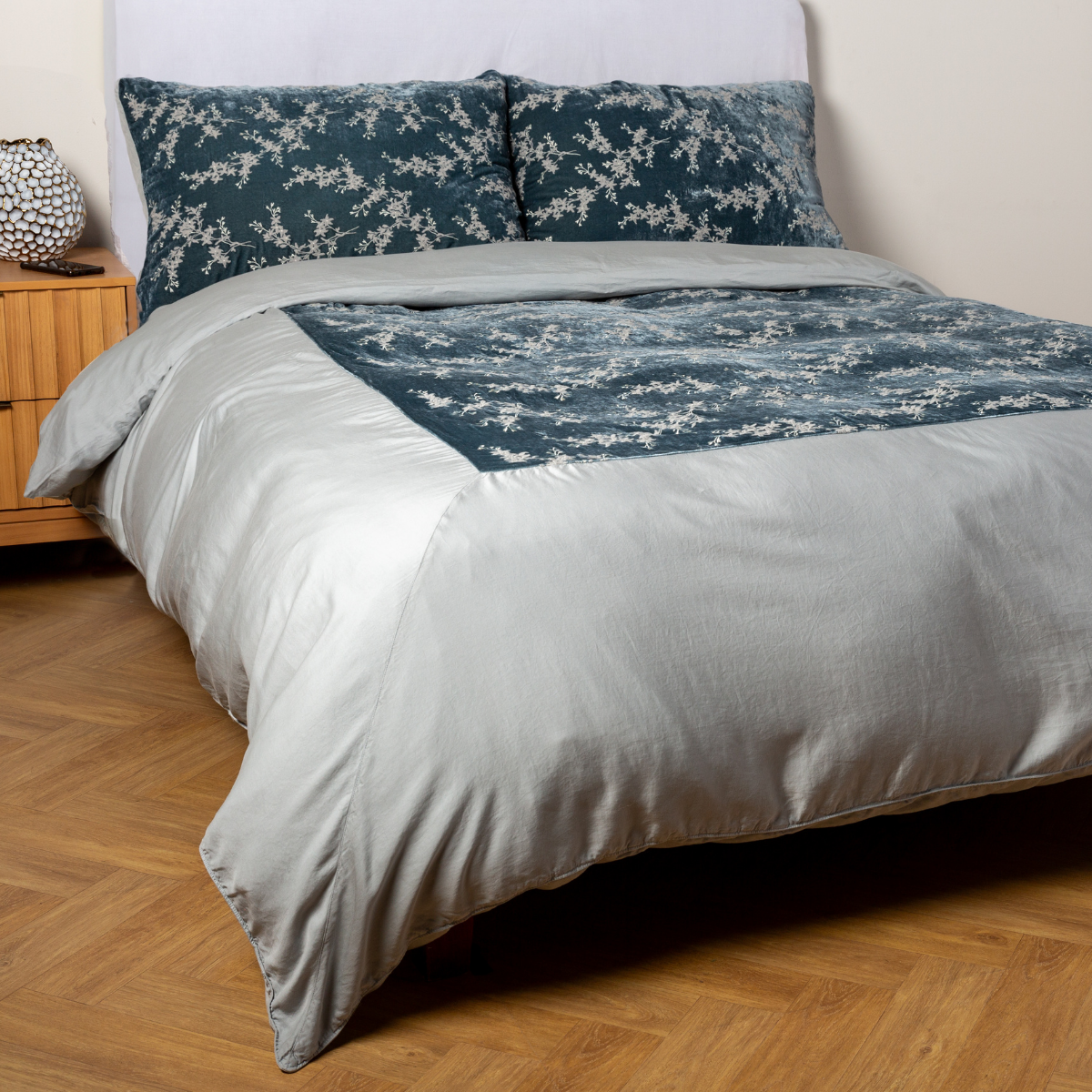 Mineral: A ¾ angle shot of an embroidered silk velvet and tencel duvet cover and matching shams with a vase and cell phone on the side table.