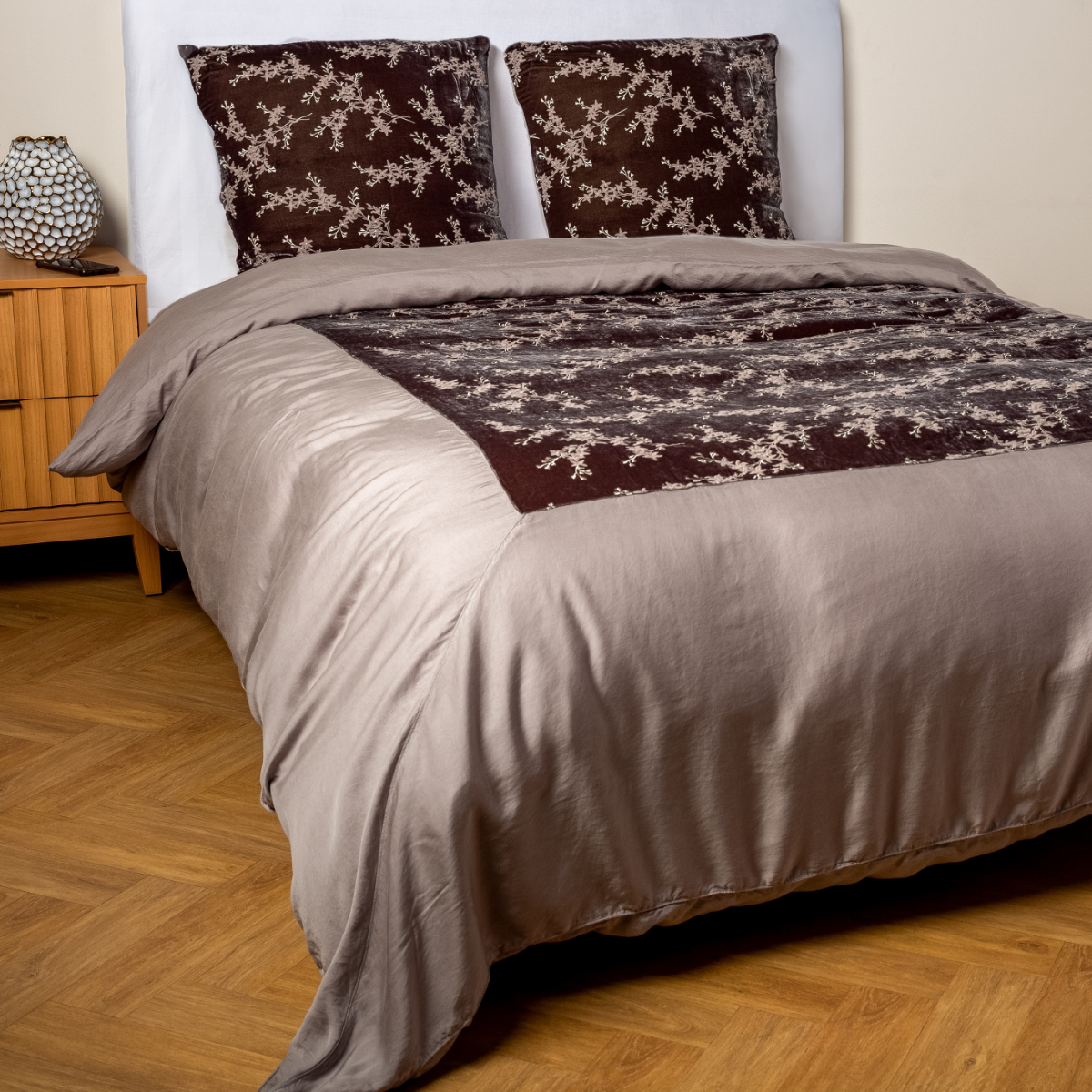 Moonlight: A ¾ angle shot of an embroidered silk velvet and tencel duvet cover and matching shams with a vase and cell phone on the side table.