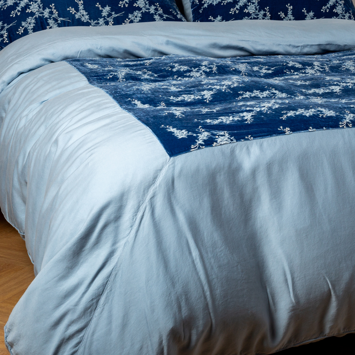Tahoe Blue: A close-up of the mitered corner of an embroidered silk velvet and tencel duvet cover — its matching shams barely visible in the shot.