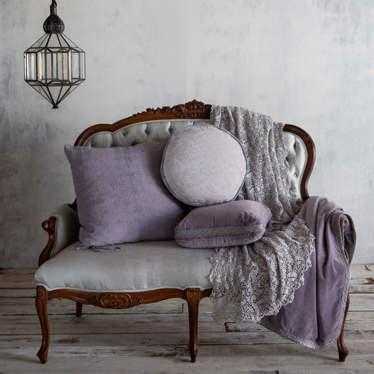 : lace bed scarf draped on a parlor sofa with an assortment of throw pillows and a cotton velvet throw blanket.