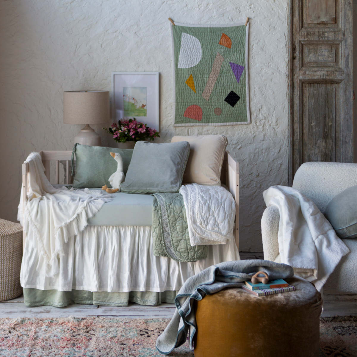 : Winter white crib skirt shown layered over a soft green crib skirt in a nursery scene with the same tones and various textures.