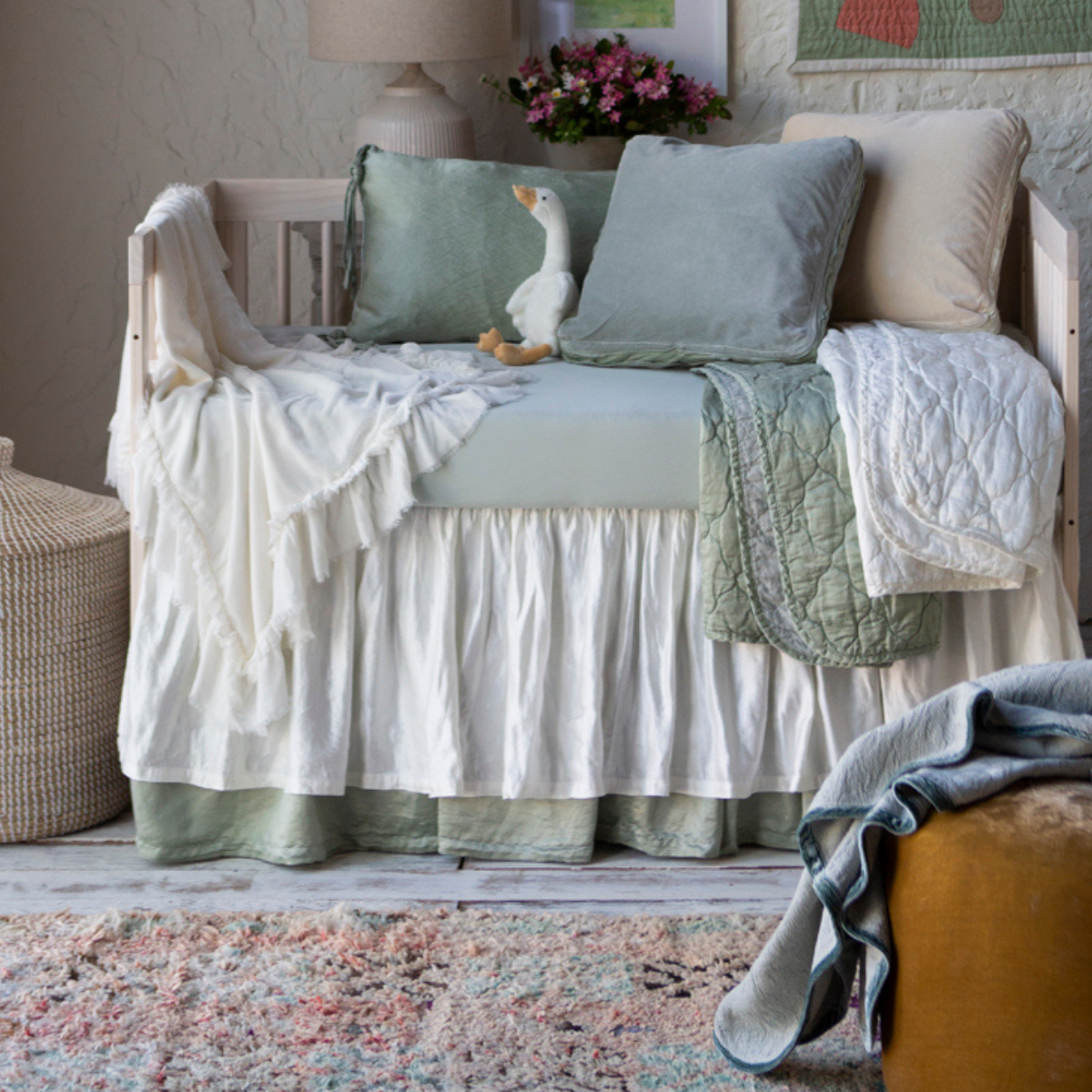 : Blanket in winter white, draped over the front and side of a crib with soft green and white bedding.