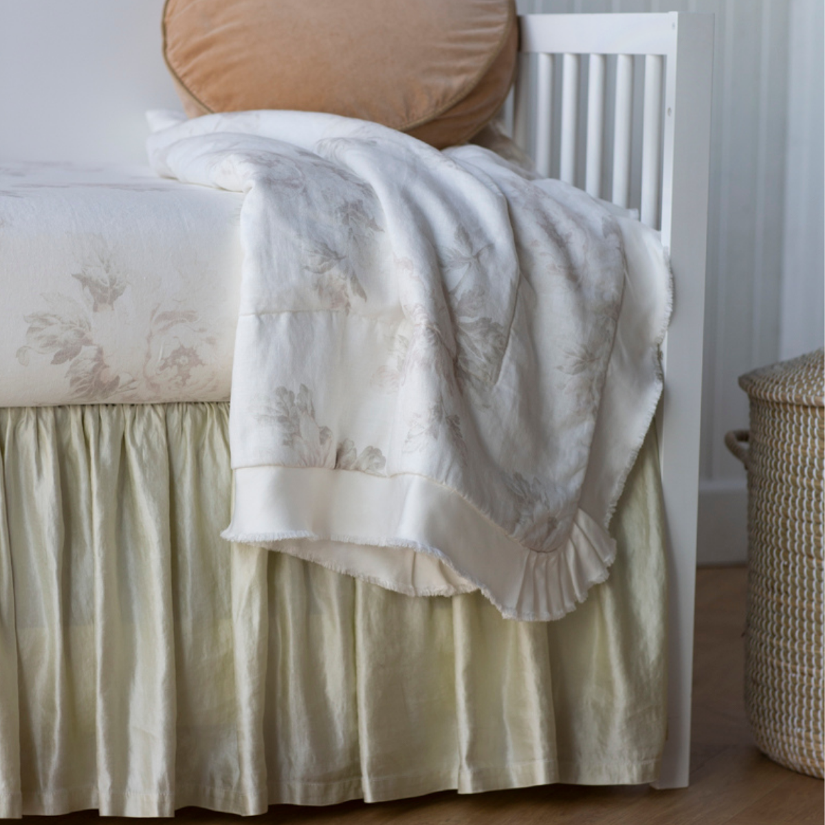 : Close up of crib skirt in parchment, shown with soft, light toned linen, showcasing the shining texture of the charmeuse.