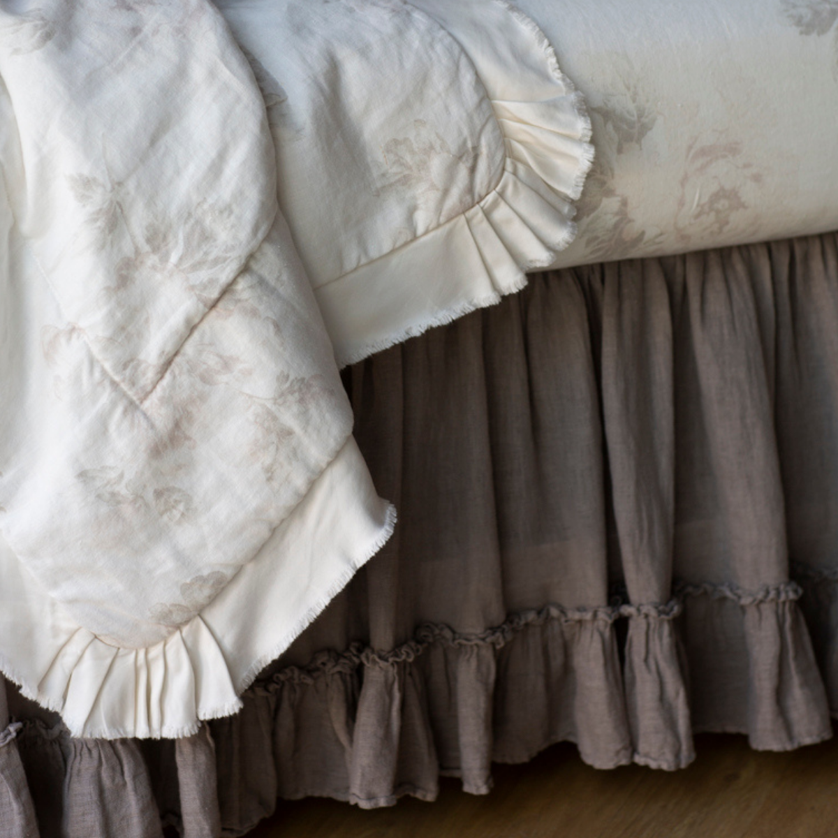 : Close up of crib skirt in moonlight under soft floral crib bedding showcases the gathering of the linen and the ruffle trim.