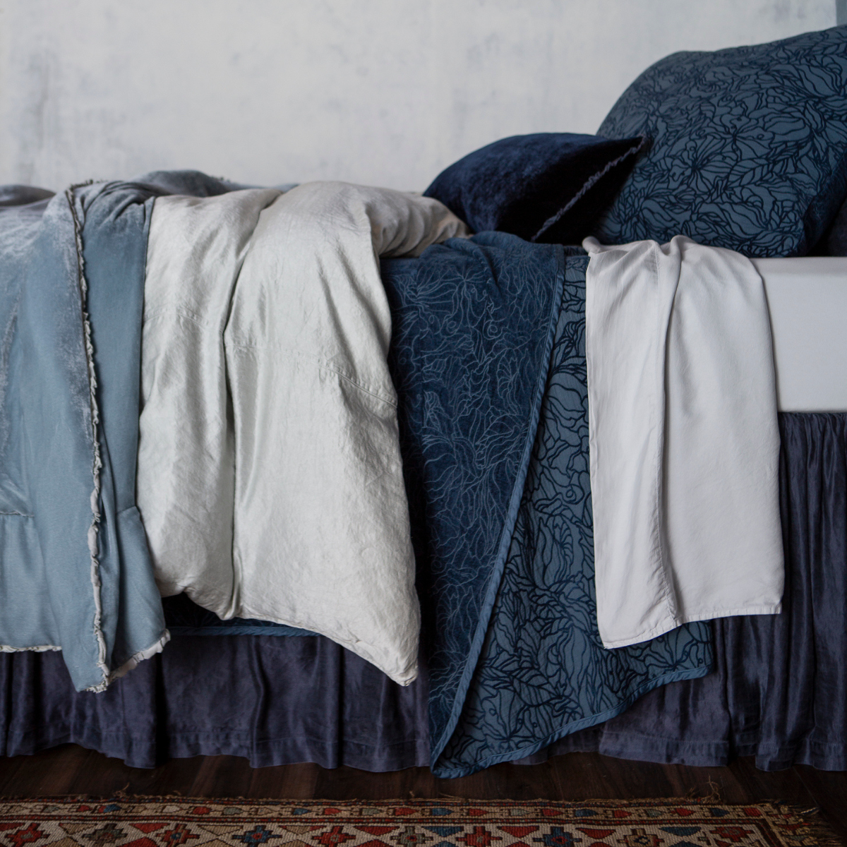 : side view of a bed dressed in various blue tones and several fabrics.