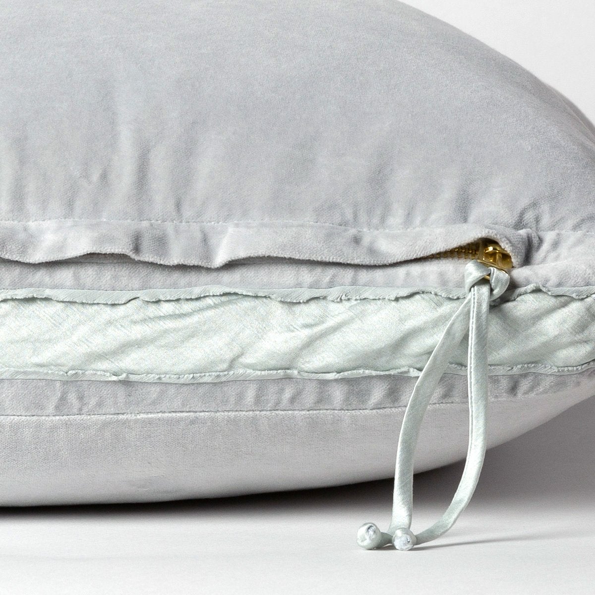 : Close-up of charmeuse gusset, raw-edge trim, and brass zipper detail on cloud Harlow pillow - cloud, side view.