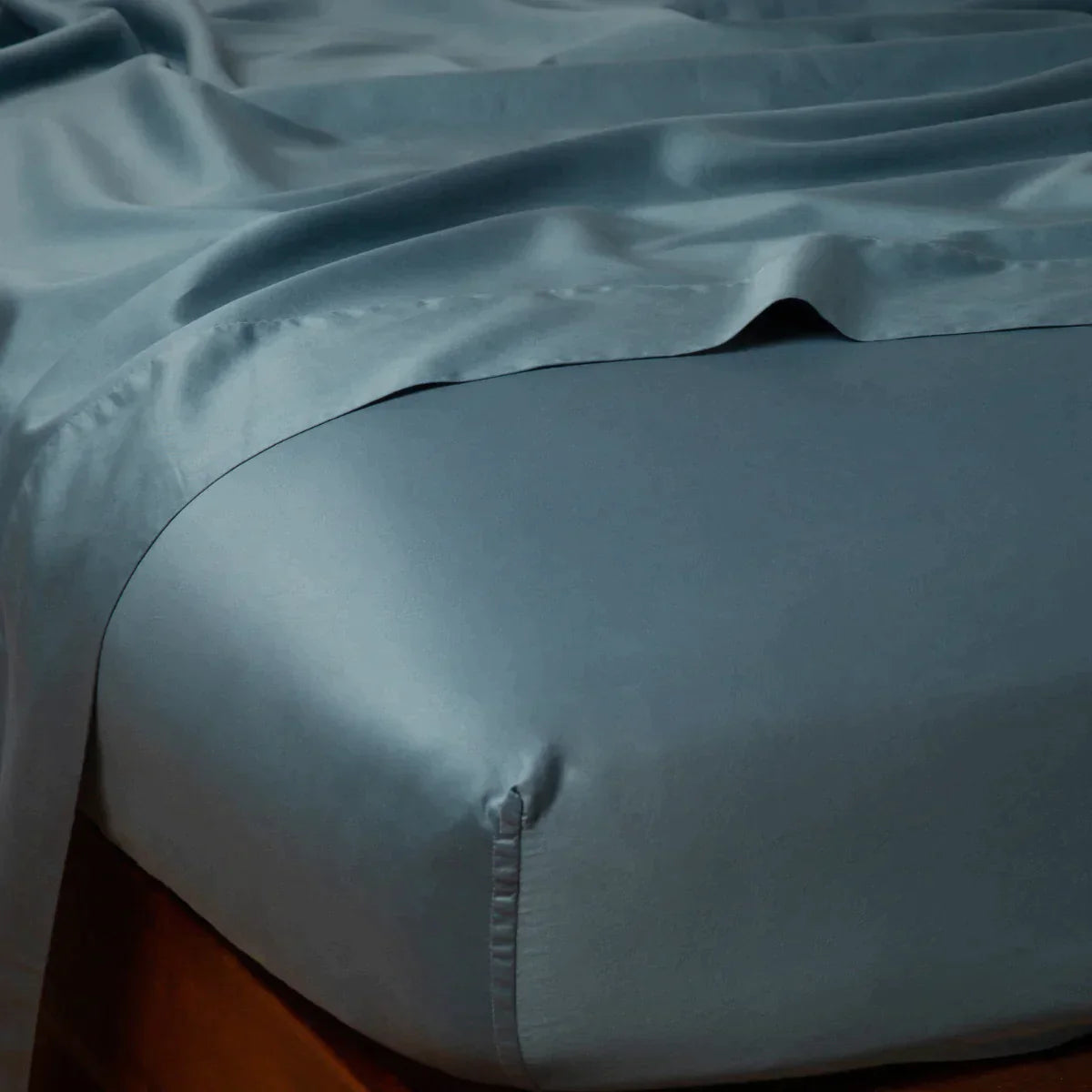 Cenote: Cotton sateen flat sheet draped over matching fitted sheet. Shown from the top corner, the flat sheet is rumpled, highlighting the shine of the fabric.