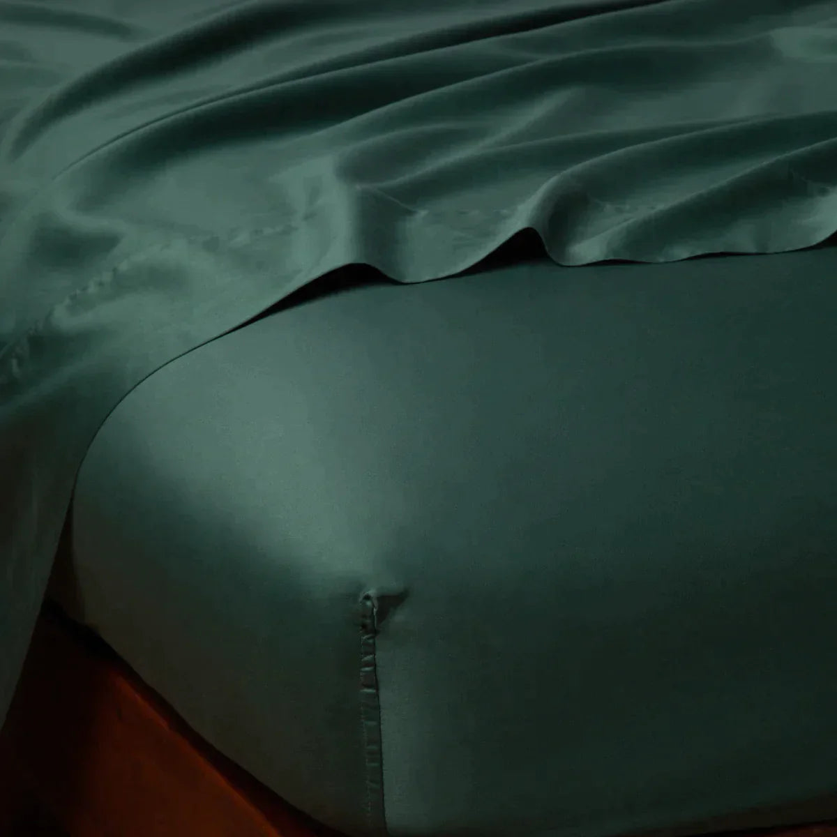 Jade: Cotton sateen flat sheet draped over matching fitted sheet. Shown from the top corner, the flat sheet is rumpled, highlighting the shine of the fabric.