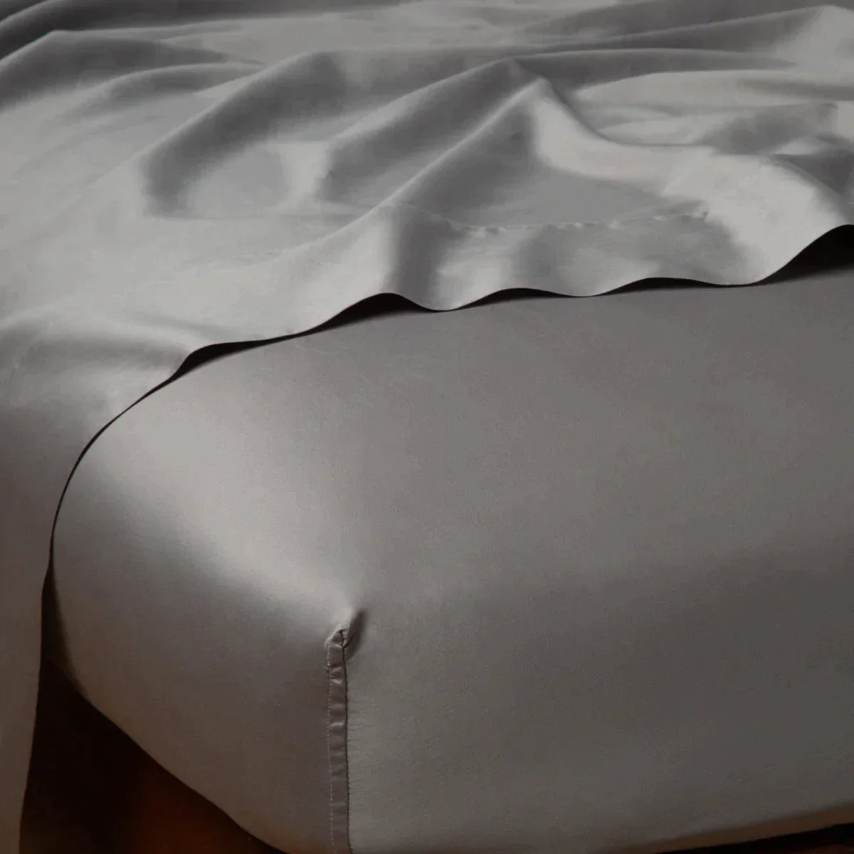Moonlight: Cotton sateen flat sheet draped over matching fitted sheet. Shown from the top corner, the flat sheet is rumpled, highlighting the shine of the fabric.