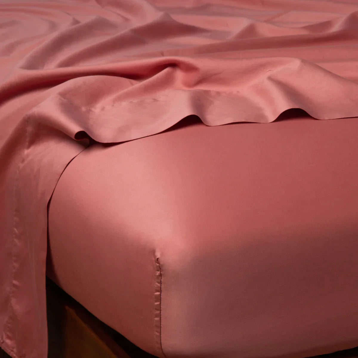 Poppy: Cotton sateen flat sheet draped over matching fitted sheet. Shown from the top corner, the flat sheet is rumpled, highlighting the shine of the fabric.