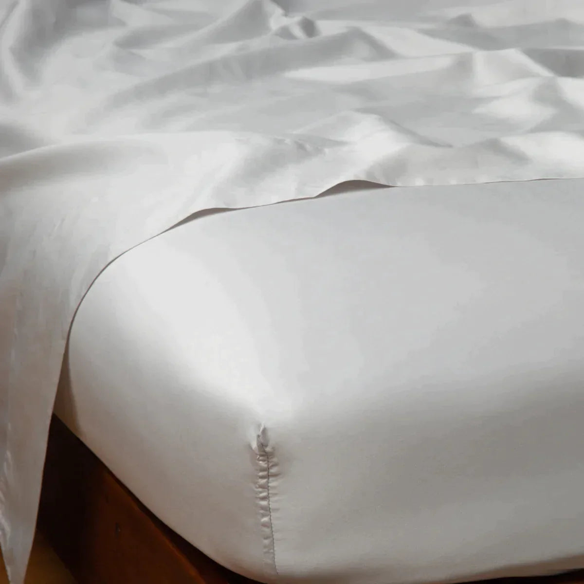 Sterling: Cotton sateen flat sheet draped over matching fitted sheet. Shown from the top corner, the flat sheet is rumpled, highlighting the shine of the fabric.
