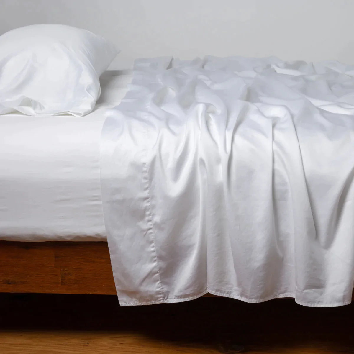 White: Cotton sateen flat sheet, shown with matching fitted sheet and sleeping pillow - side view.