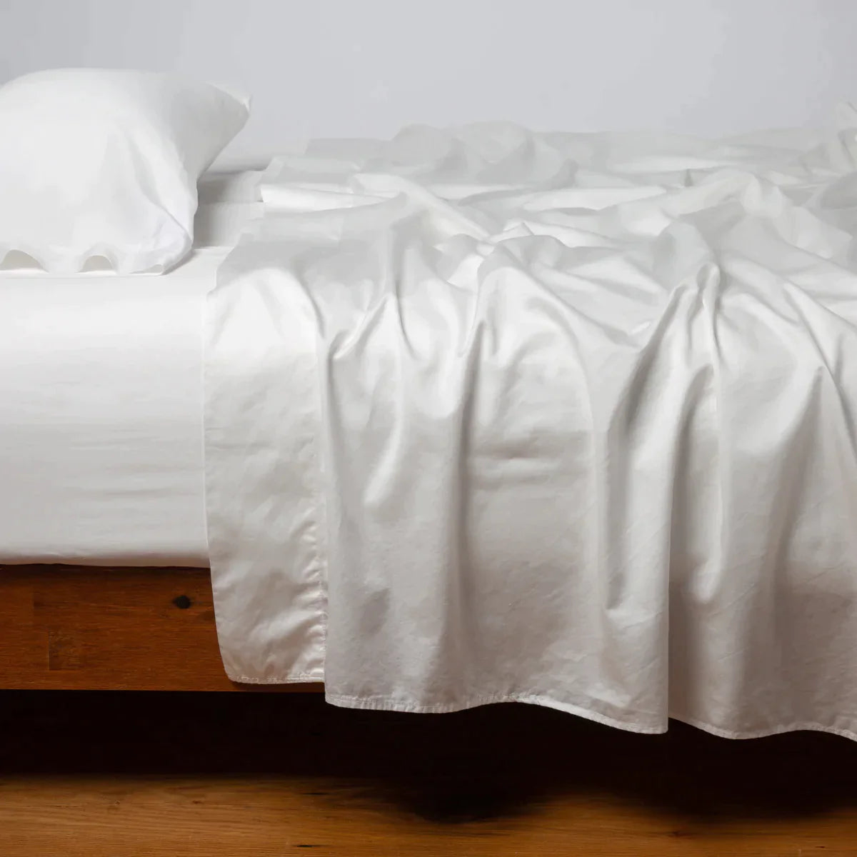 Winter White: Cotton sateen flat sheet, shown with matching fitted sheet and sleeping pillow - side view.