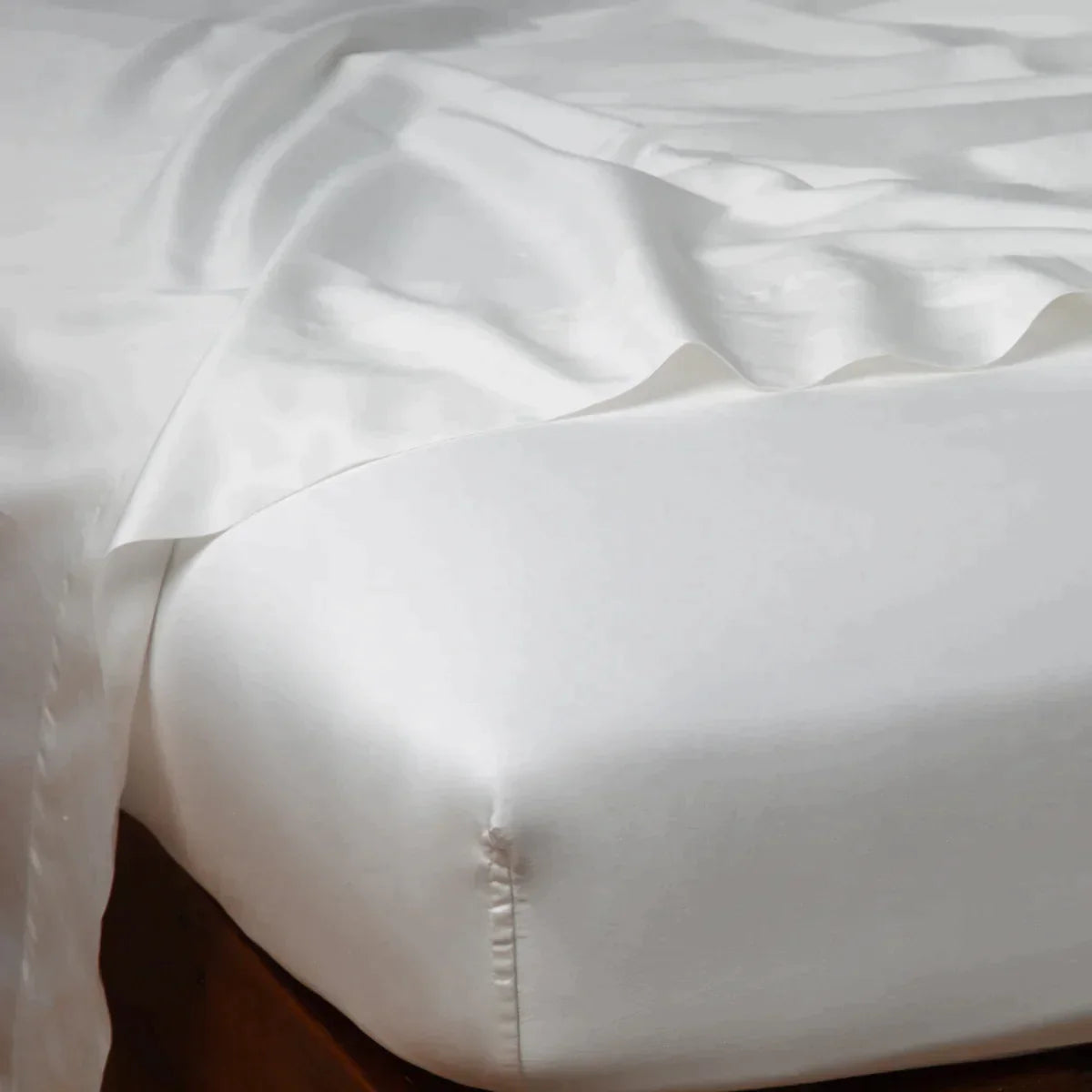 Winter White: Cotton sateen flat sheet draped over matching fitted sheet. Shown from the top corner, the flat sheet is rumpled, highlighting the shine of the fabric.
