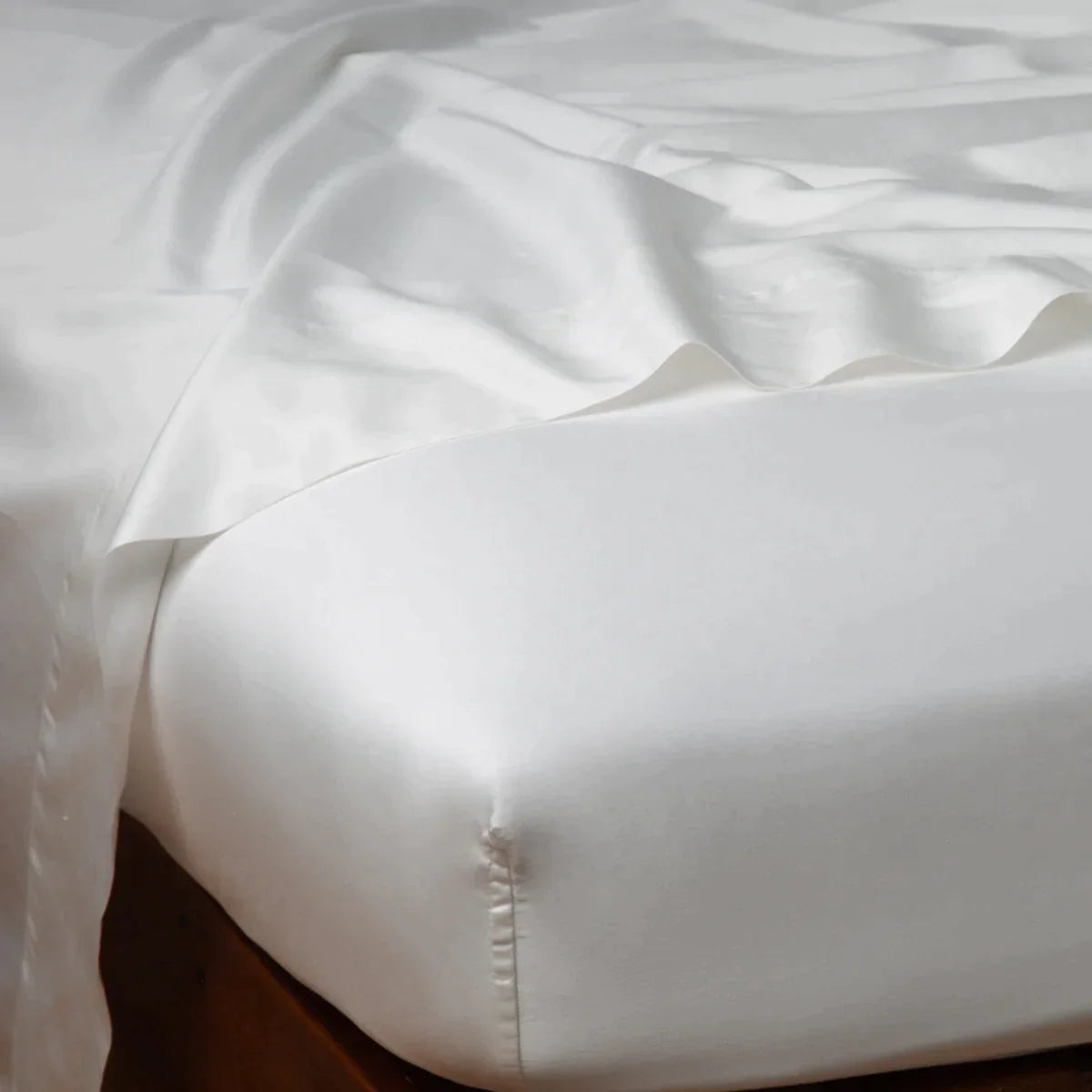 Winter White: Cotton sateen flat sheet draped over matching fitted sheet. Shown from the top corner, the flat sheet is rumpled, highlighting the shine of the fabric.