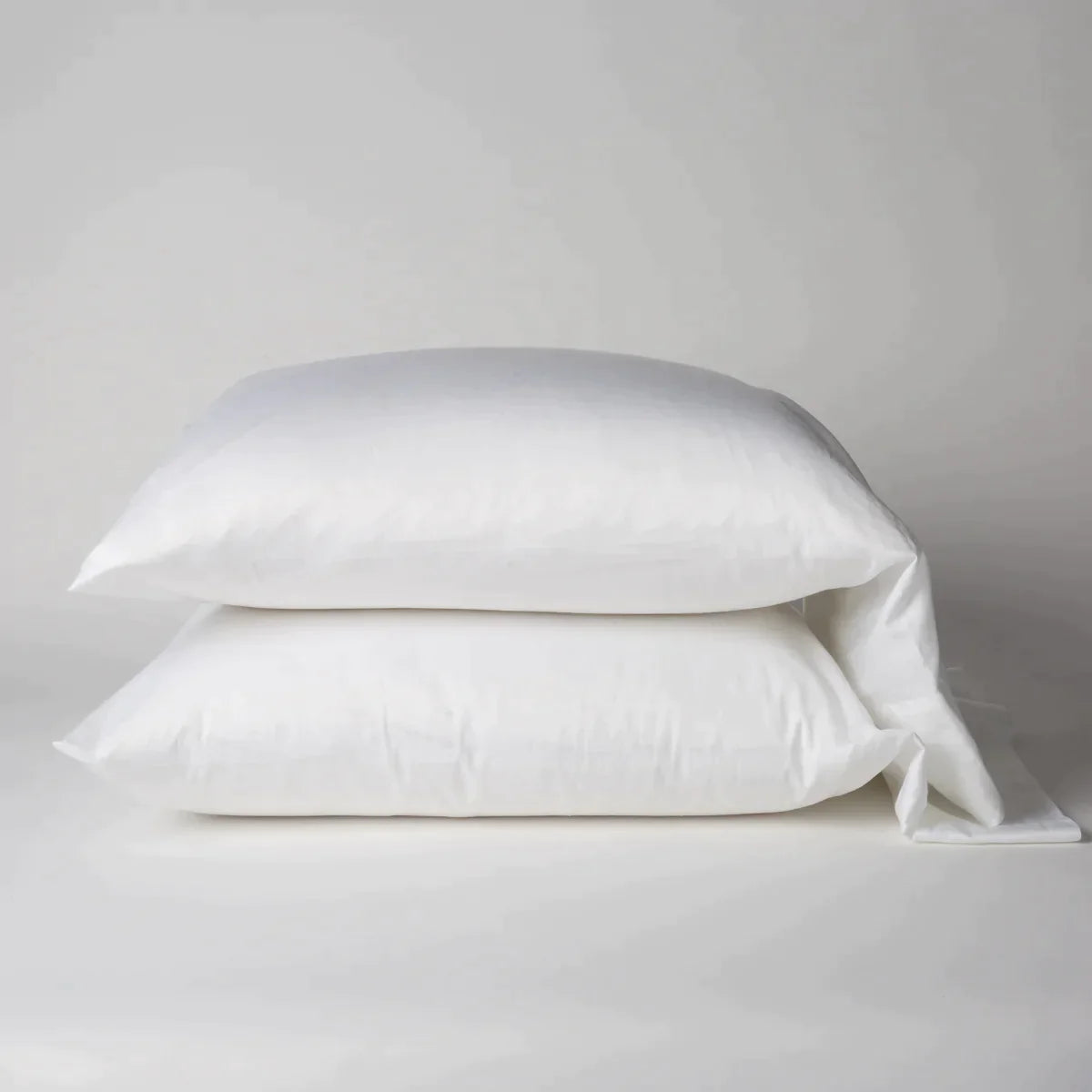 White: Two cotton sateen sleeping pillows, stacked neatly against a white backdrop - side view.