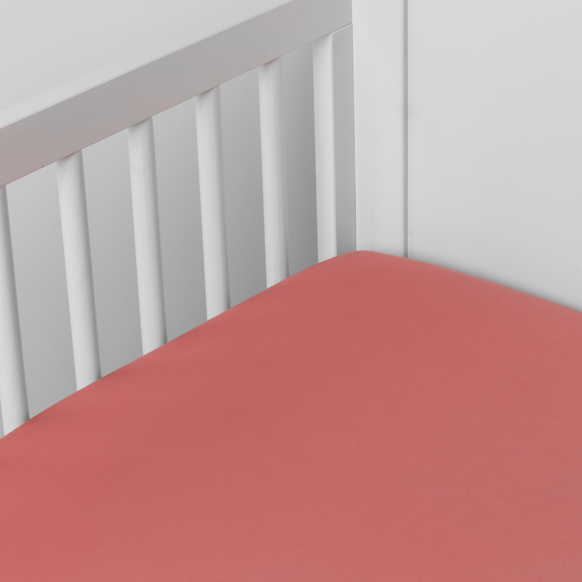 Poppy: Cotton sateen crib sheet shown from a slight overhead angle into an inside corner of a crib.
