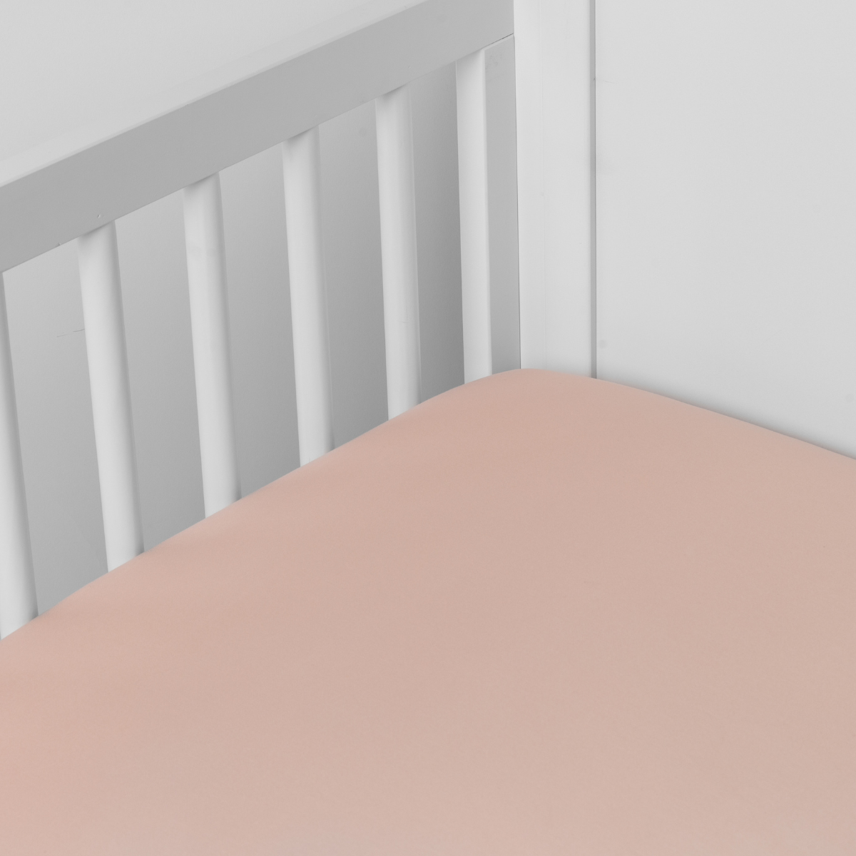 Rouge: Cotton sateen crib sheet shown from a slight overhead angle into an inside corner of a crib.