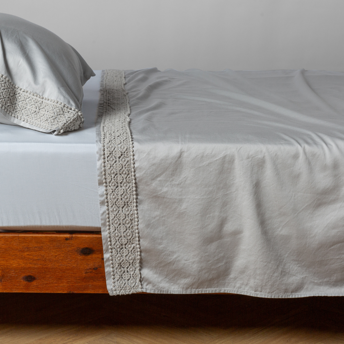 Matching lace trimmed cotton sateen flat sheet and pillowcase shown with a winter white fitted sheet - side view.