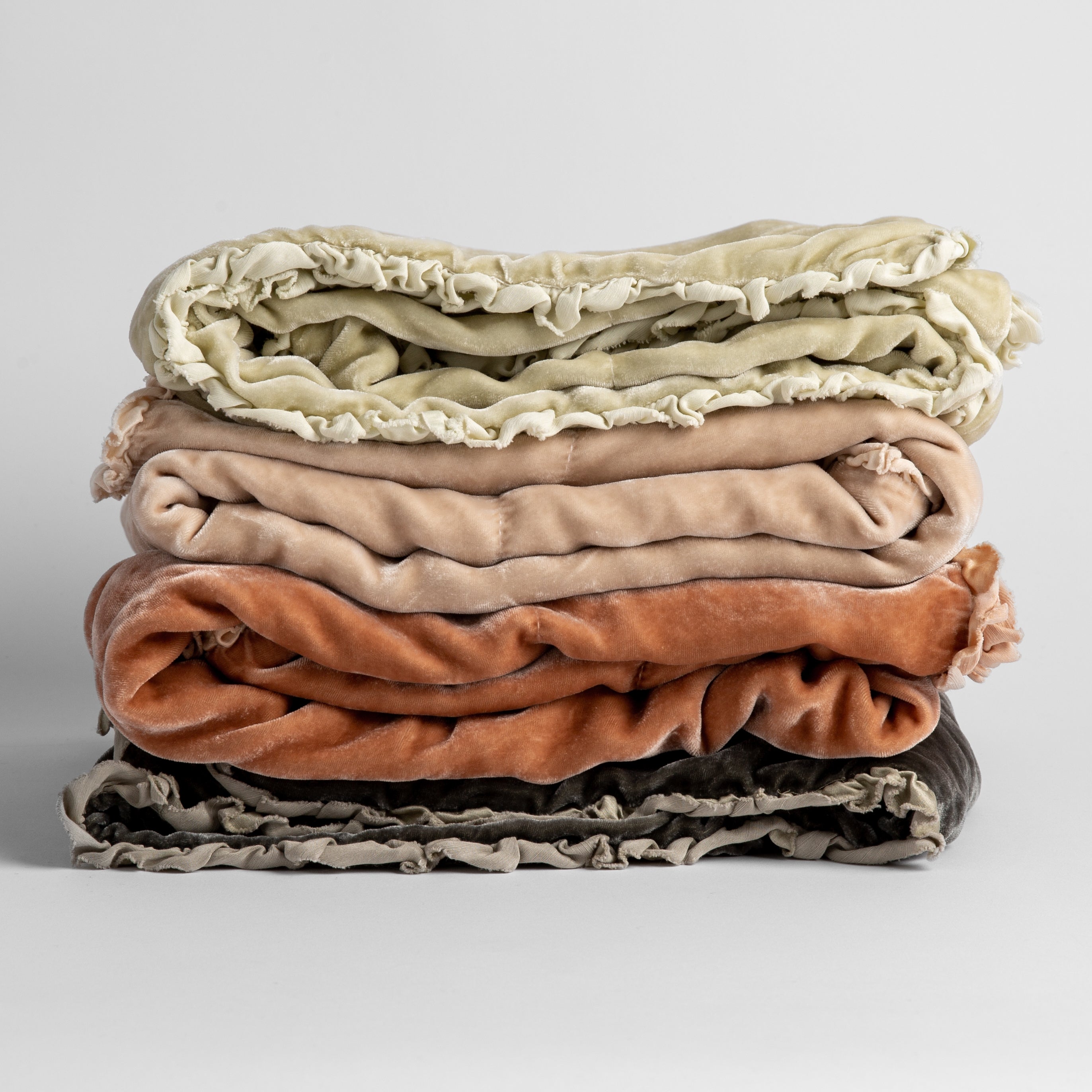 : stack of four silk velvet baby blankets with charmeuse trim shown against a white background. Blankets shown in Parchment, Pearl, Rouge and Fog.