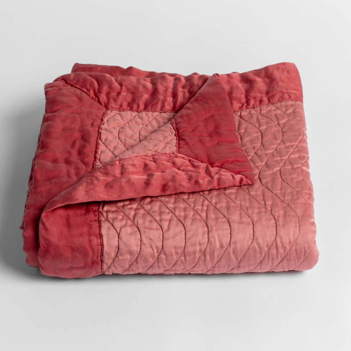 Poppy: a folded quilted cotton sateen baby blanket with its corner folded down to show the trim contrast - shot against a white background.