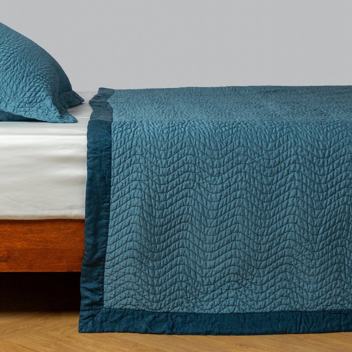 Cenote: quilted cotton sateen coverlet with matching sham on a winter white fitted sheet - side view.