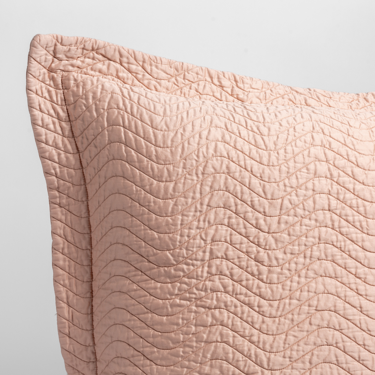 Rouge: close up of the corner of a quilted cotton sateen pillow sham - shot against a white background.
