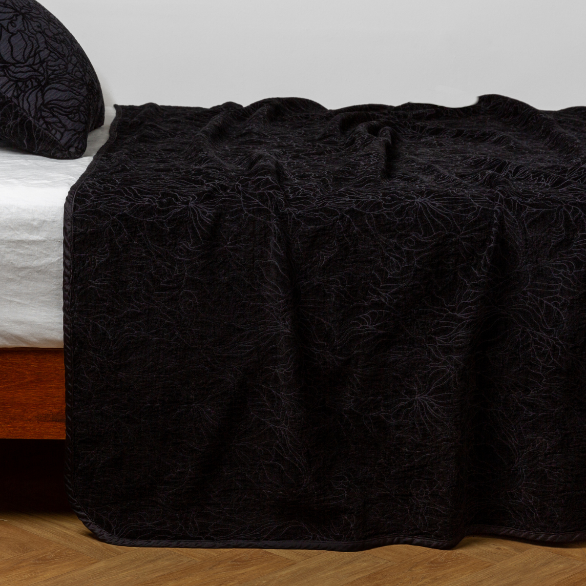 Corvino: side view of the chenille jacquard side of a bedspread with the cotton jacquard side showing on the matching sham — shown with a winter white fitted sheet.