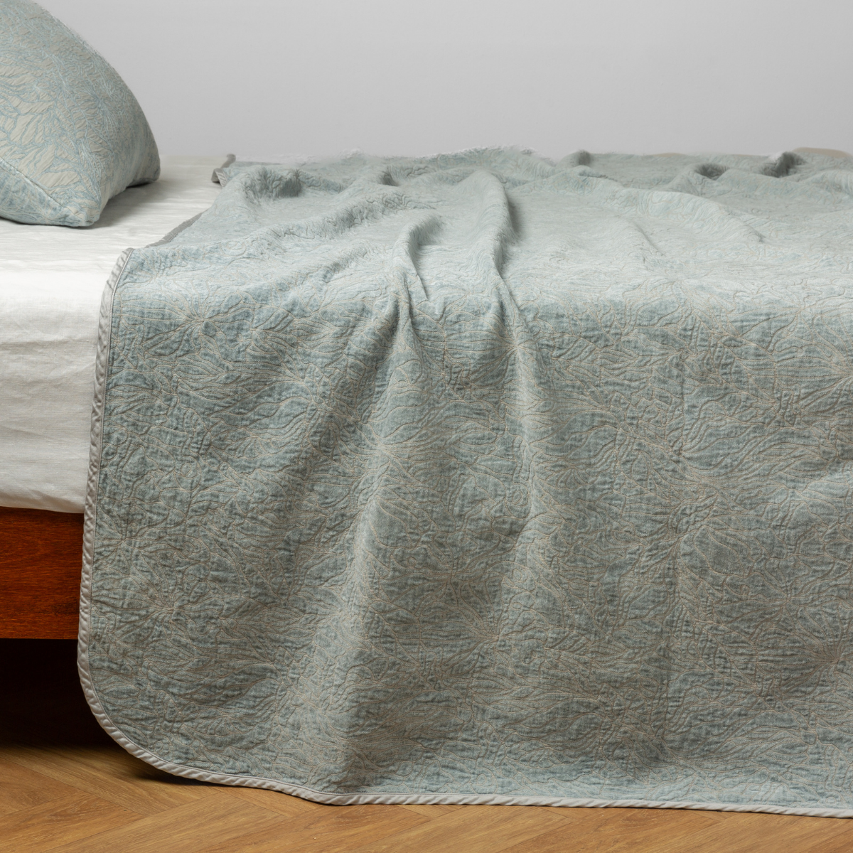 Eucalyptus: side view of the chenille jacquard side of a bedspread with the cotton jacquard side showing on the matching sham — shown with a winter white fitted sheet.