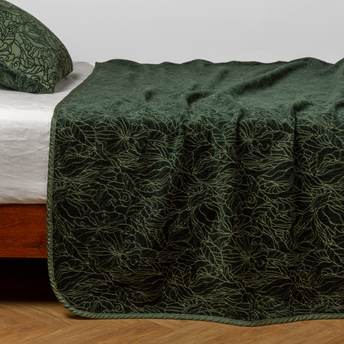 Juniper: side view of the chenille jacquard side of a bedspread with the cotton jacquard side showing on the matching sham — shown with a winter white fitted sheet.