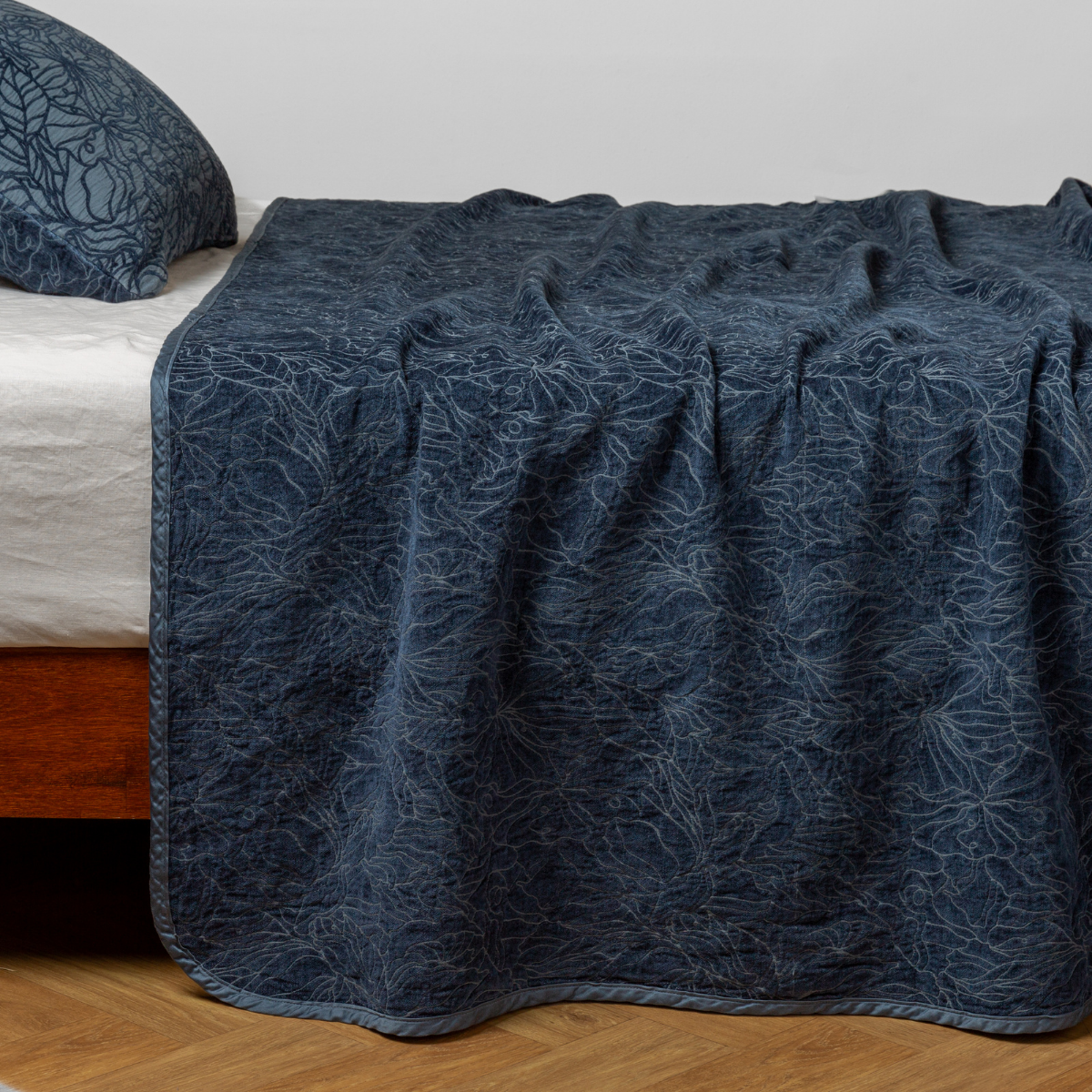Midnight: side view of the chenille jacquard side of a bedspread with the cotton jacquard side showing on the matching sham — shown with a winter white fitted sheet.