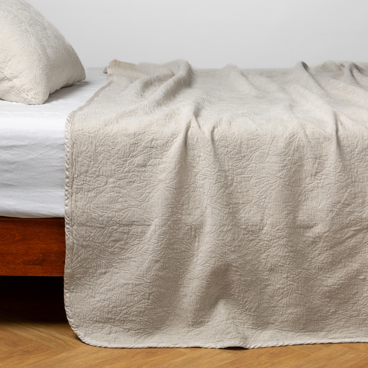 Parchment: side view of the chenille jacquard side of a bedspread with the cotton jacquard side showing on the matching sham — shown with a winter white fitted sheet.