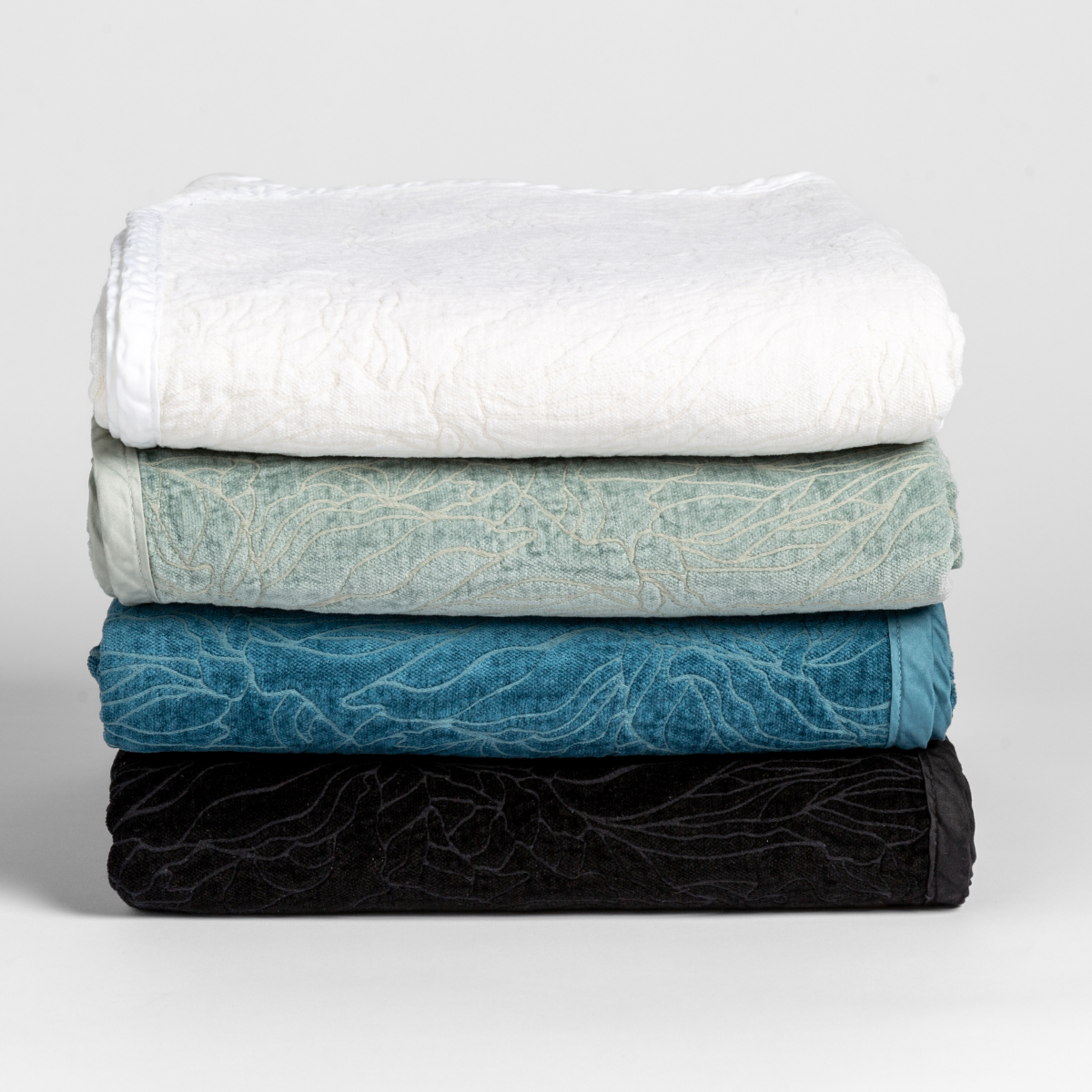 : a stack of four blankets folded with their chenille jacquard sides facing outward and the cotton sateen trim subtle and tonal.