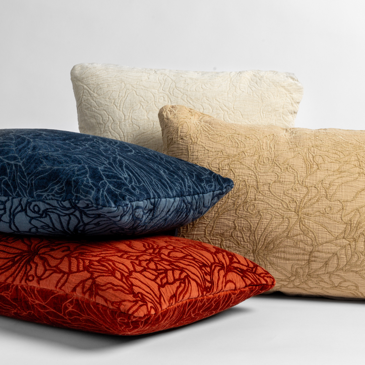 Four Georgia throw pillows shown in a fun array against a white background on either their chenille jacquard or cotton jacquard sides in the following colorways: Winter White, a wooly and warm tone, Honeycomb, a golden hue, Midnight, a rich indigo, and Autumn, a rich terracotta tone.