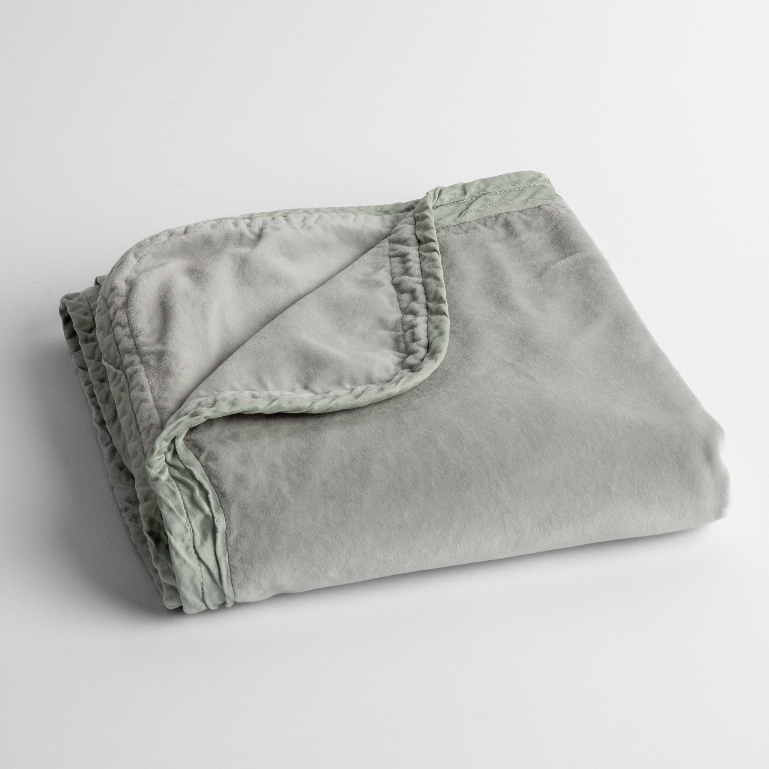 Cloud: cotton velvet baby blanket trimmed with charmeuse, folded with a covern folded back to show trim contrast; shot overhead and at a slight angle against a white background.