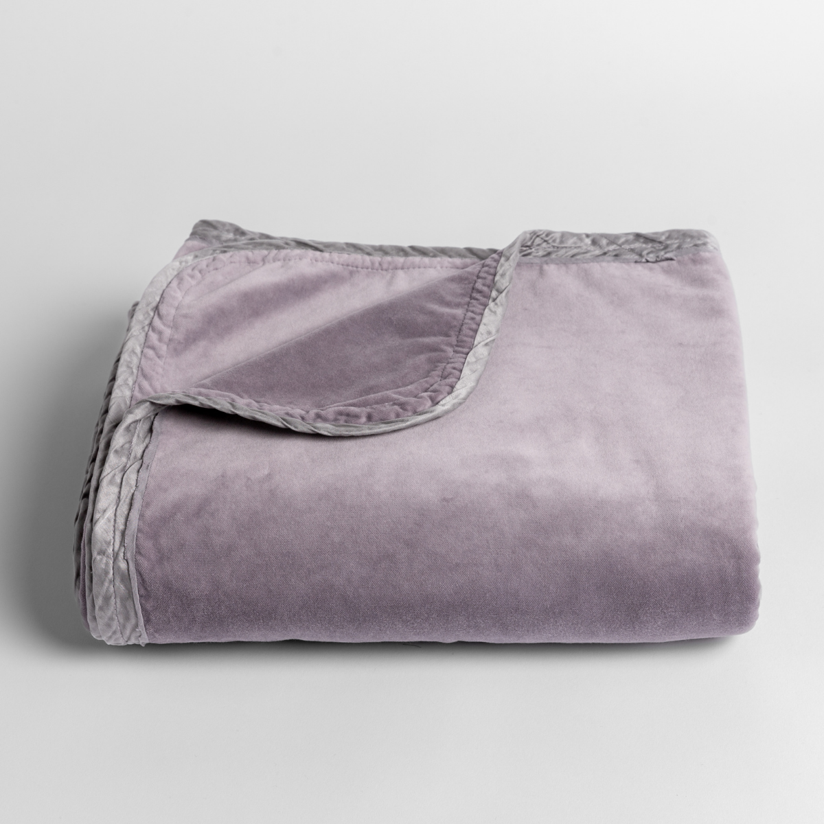 French Lavender: cotton velvet baby blanket trimmed with charmeuse, folded with a corner folded back to show trim contrast; shot overhead at a slight angle against a white background.