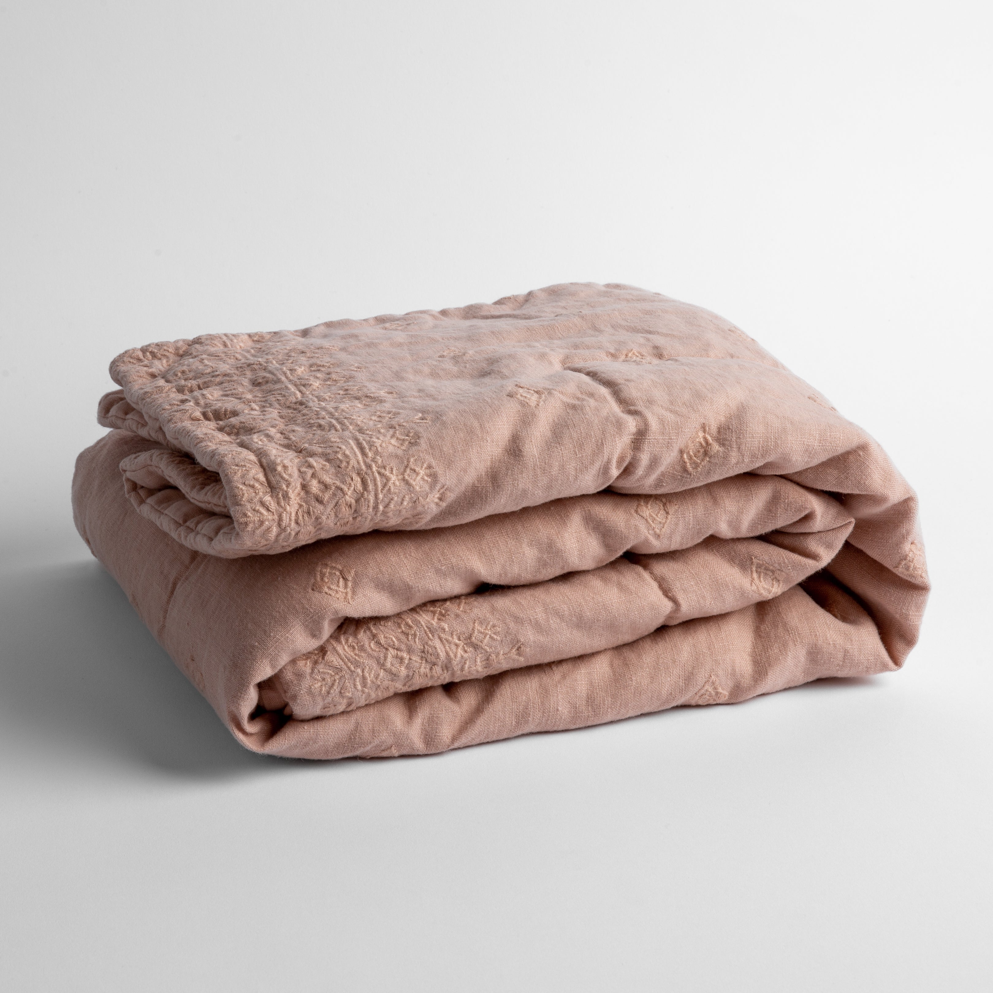 Rouge: embroidered linen baby blanket folded and shown overhead from a slight angle against a white background.