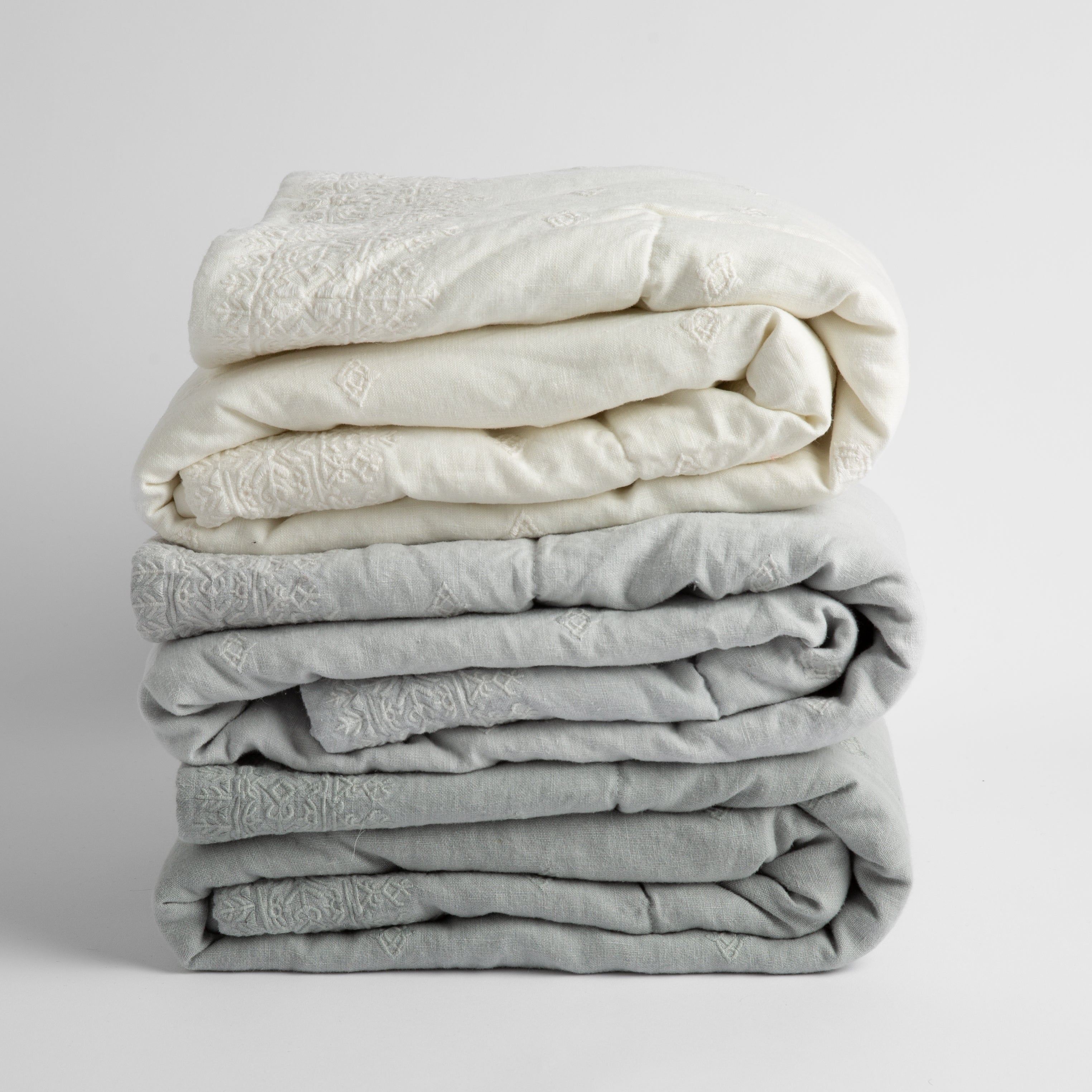 a stack of three embroidered linen baby blankets in cool tones: winter white, cloud and eucalyptus