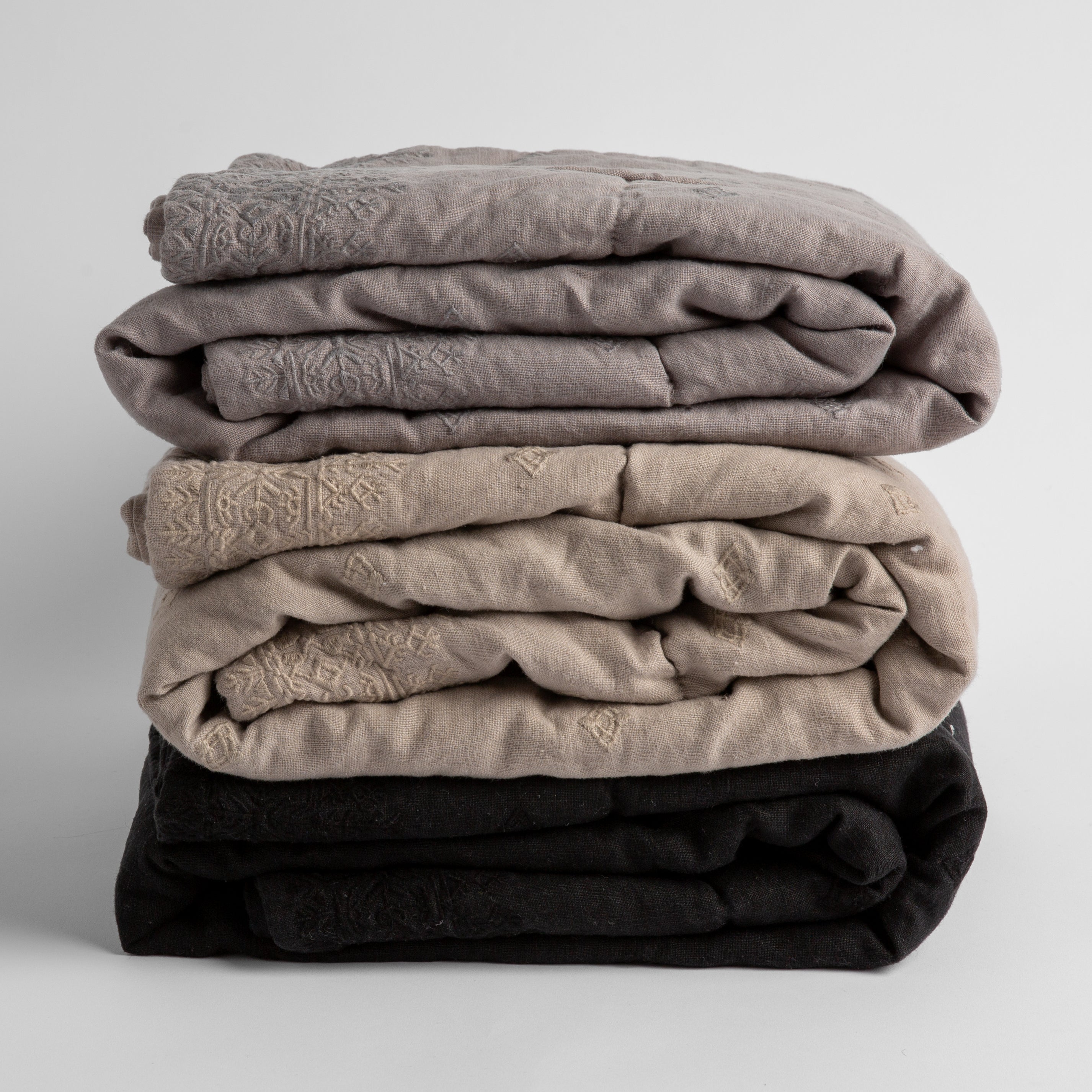 A stack of three embroidered linen baby blankets in moonlight, fog and corvino.