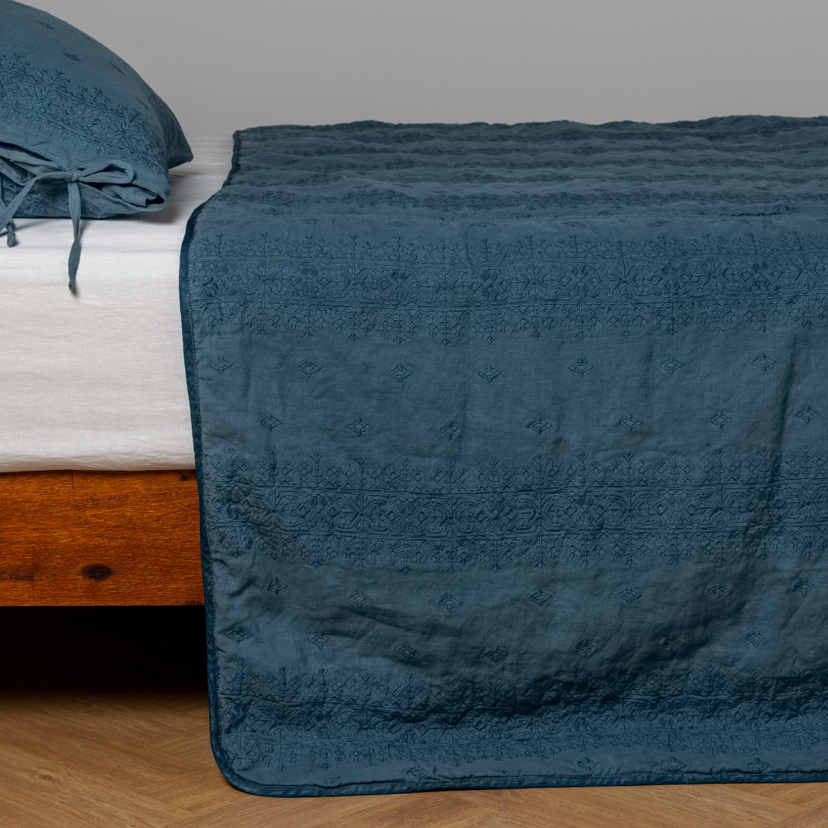 Cenote: embroidered midweight linen bedspread with matching sham on a bed with a white fitted sheet. Shot from the side view, the bedframe is slightly visible against a white background and medium wood floor.