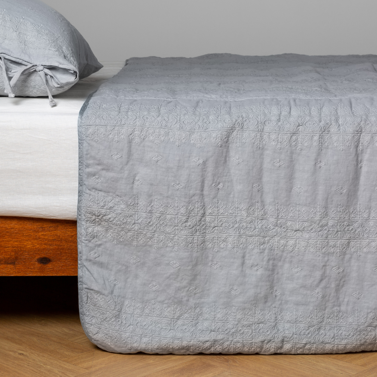 Cloud: embroidered midweight linen bedspread with matching sham on a bed with a white fitted sheet. Shot from the side view, the bedframe is slightly visible against a white background and medium wood floor.