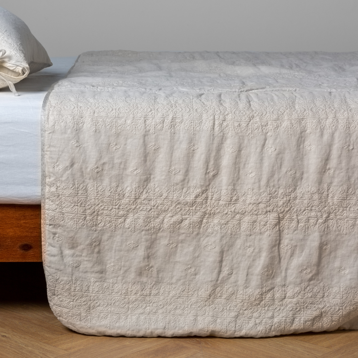 Parchment: embroidered midweight linen bedspread with matching sham on a bed with a white fitted sheet. Shot from the side view, the bedframe is slightly visible against a white background and medium wood floor.