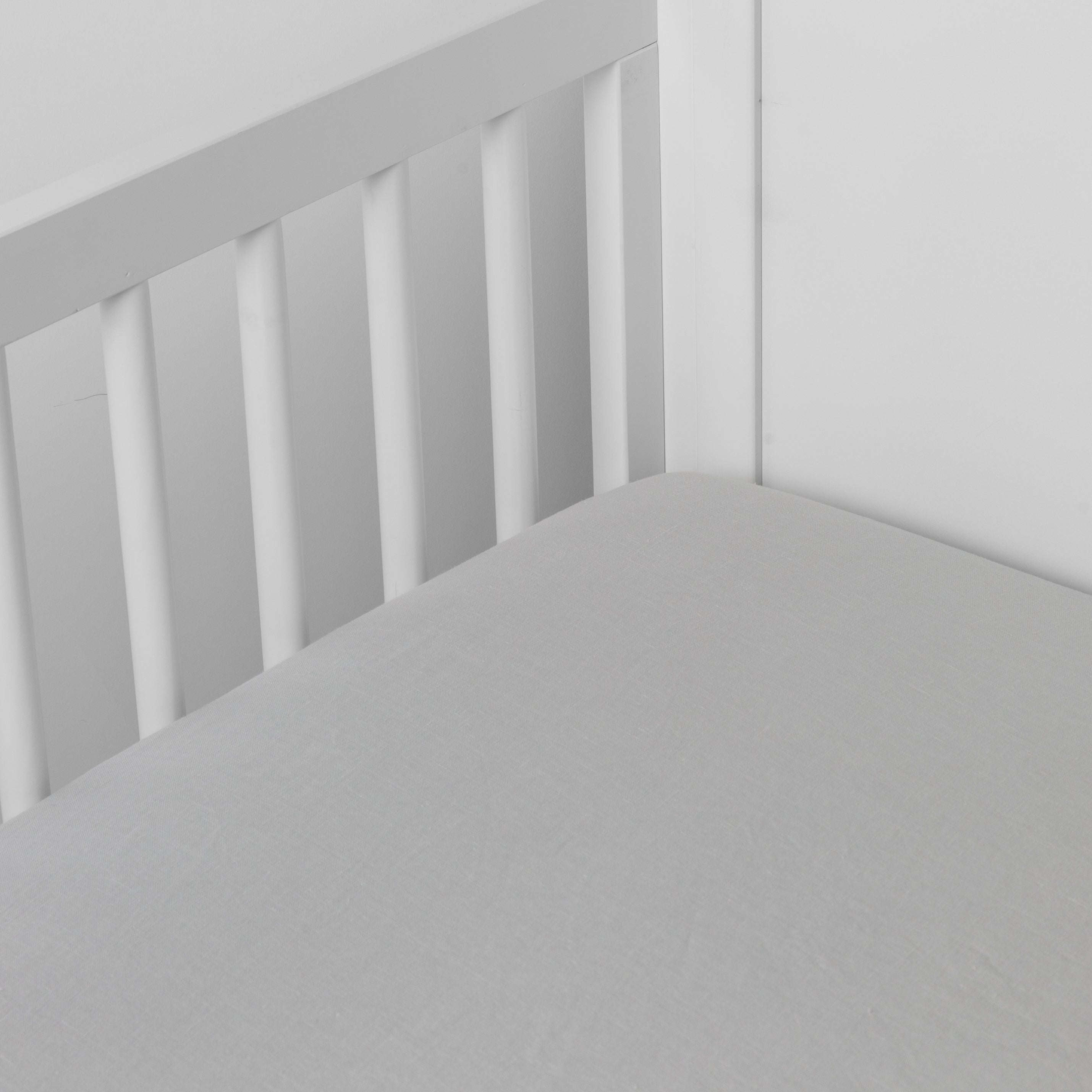 Cloud: linen crib sheet on the mattress shot slightly overhead into the corner of a white crib. against a white background.