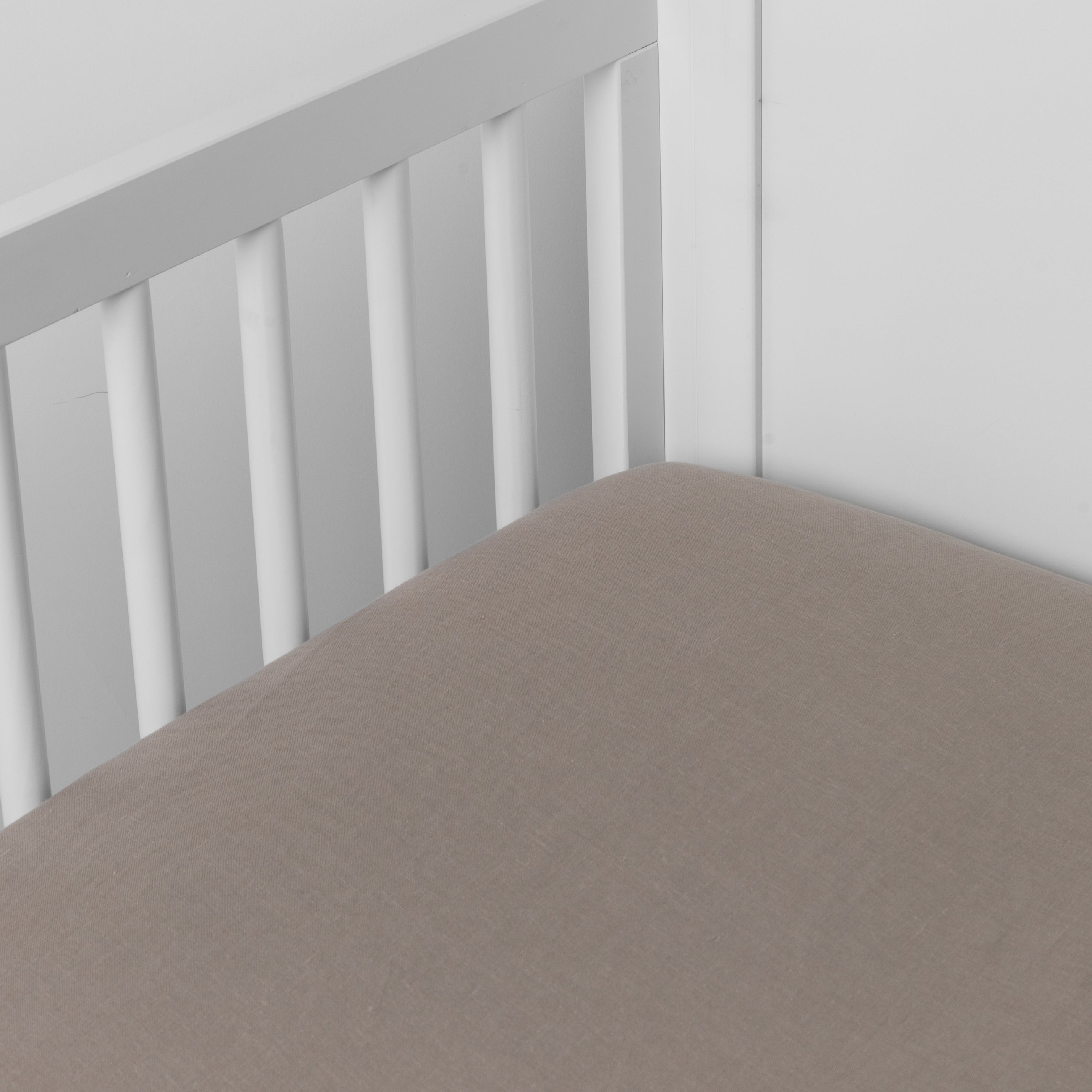 Fog: linen crib sheet on the mattress shot slightly overhead into the corner of a white crib. against a white background.